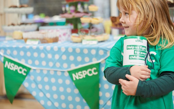 A young girl smiling while holding an NSPCC collection box.