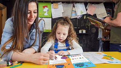 long haired white  woman helps young white girl with activity book