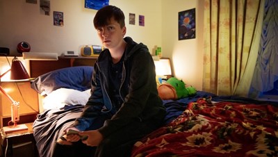 Photograph of a young adult sat on their bed.