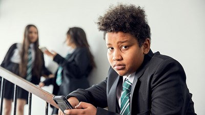 A secondary school pupil on a mobile phone while staring blankly into the distance.