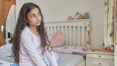 A young child sat on their bed staring blankly into the distance.