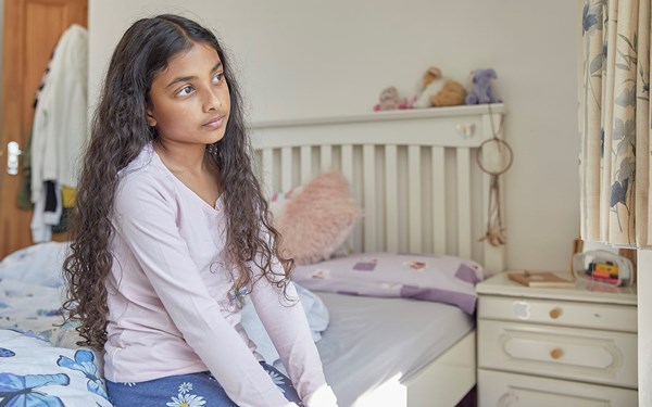 A young child sat on their bed staring blankly into the distance.