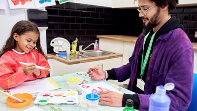 A young child smiling while painting with an NSPCC service practitioner.