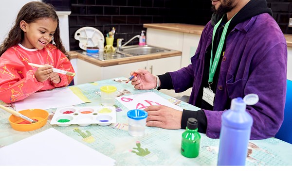 A young child smiling while painting with an NSPCC service practitioner.
