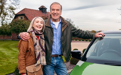 Two lottery winners smiling in front of their new car.