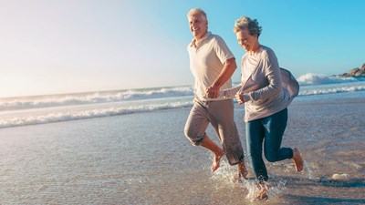 A couple smiling and laughing while running on a beach.