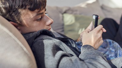 A teenager lay down while using their mobile.