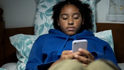 A teenager sat on their bed while using their mobile.