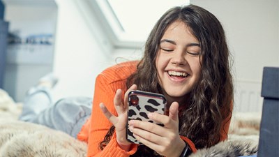 A teenager smiling while using their mobile phone.