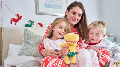 A mother and her two young children opening Christmas presents together.