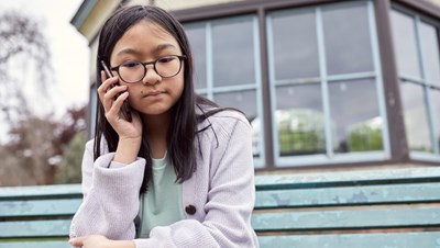 Photograph of a child sat outside making a call on their mobile phone.
