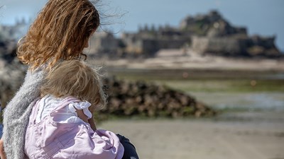 A young girl and a toddler hugging on a beach.