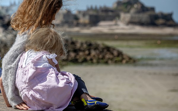 A young girl and a toddler hugging on a beach.