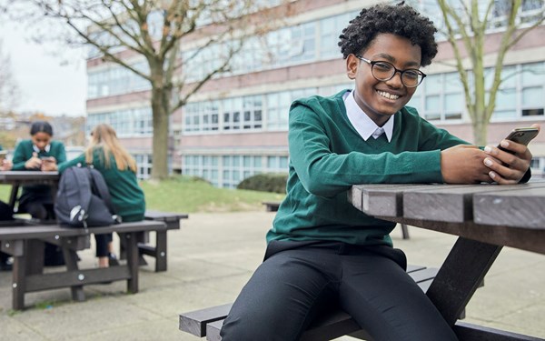 A teenager happily using a mobile phone at school.