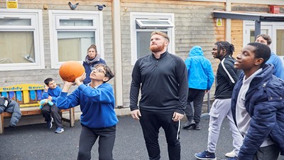 Young boy playing basketball with coach in playground