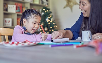 Young girl writing and smiling beside Christmas tree