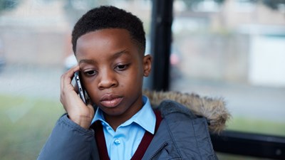 A young boy talking on the phone at a bus stop