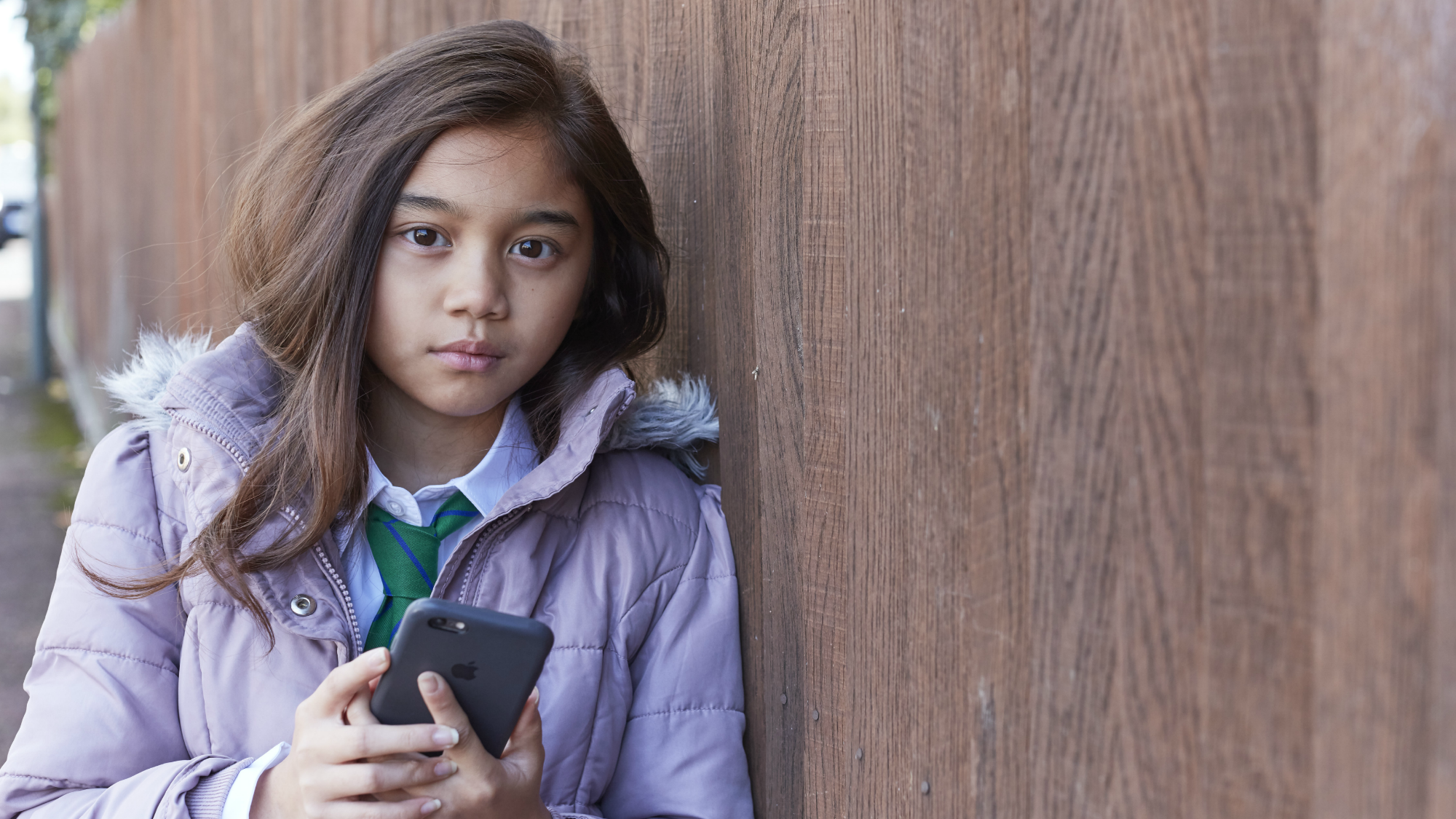 Young girl leaning against fence, holding phone