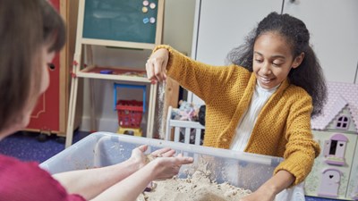 Young girl smiling and playing with sand.