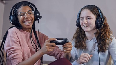 Two teenage girls smiling while playing a video game together.