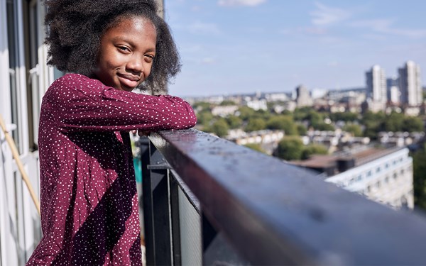 A teenage girl on a balcony smiling into the camera.