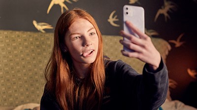 A teenager posing while taking a selfie on their mobile phone.