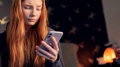 A teenager looking worried while using their mobile phone.