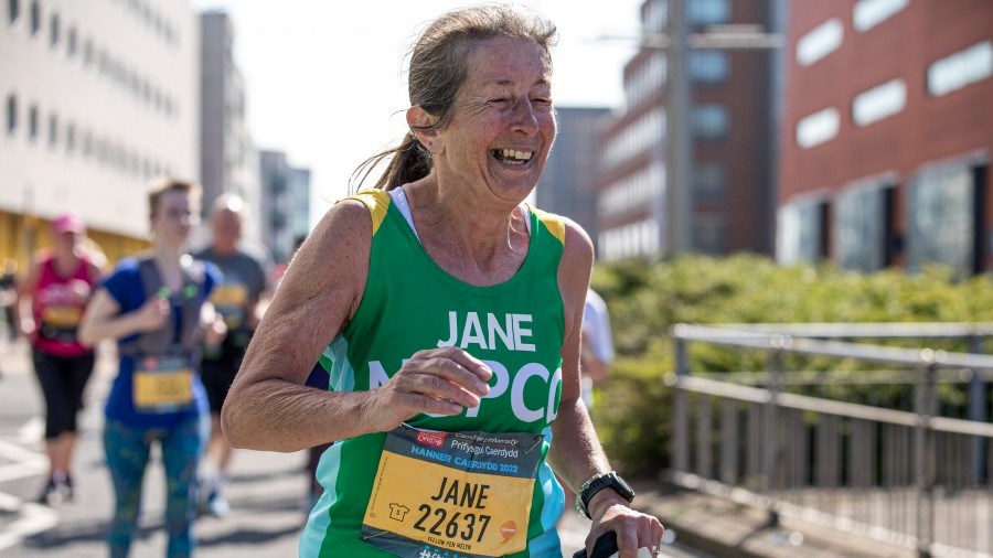 Cardiff Half runner in NSPCC vest, smiling as they run along