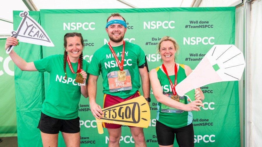 A group of three NSPCC runners, wearing their finisher medals, hold up signs saying yeah and let's go
