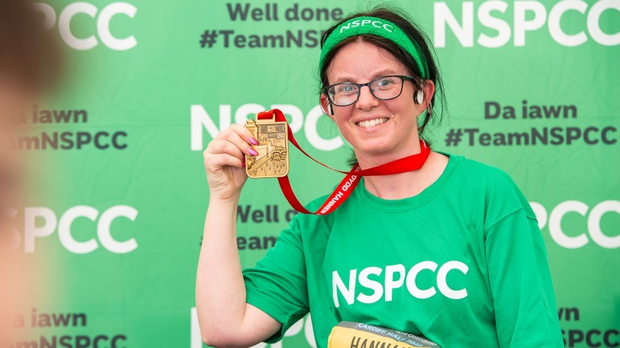An NSPCC Cardiff Half runner, in front of the charity's stand, holds up their finisher medal