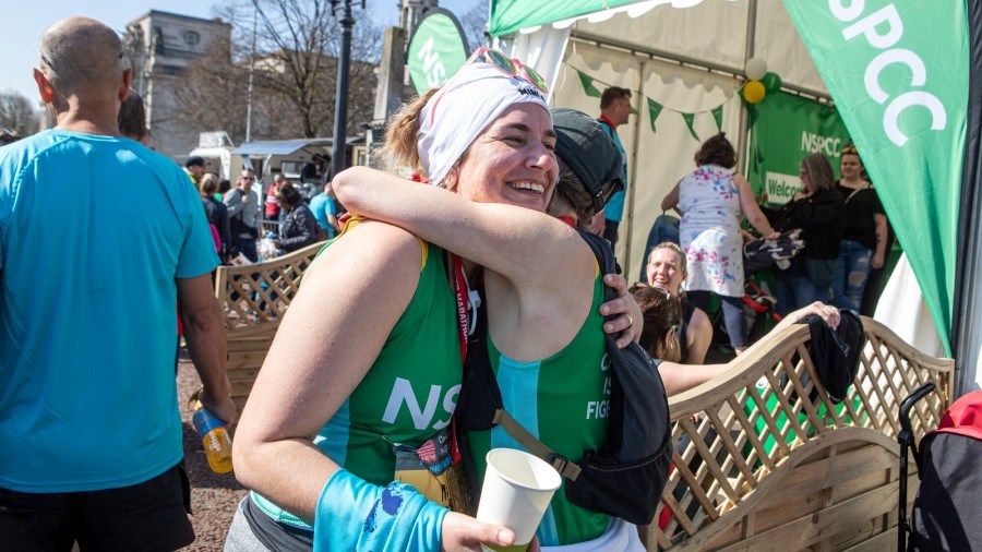 Two Cardiff Half runners, wearing NSPCC vests, hug one another 