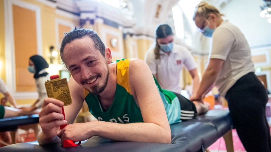 An NSPCC Cardiff Half runner on the physiotherapy table, holding up their medal to the camera