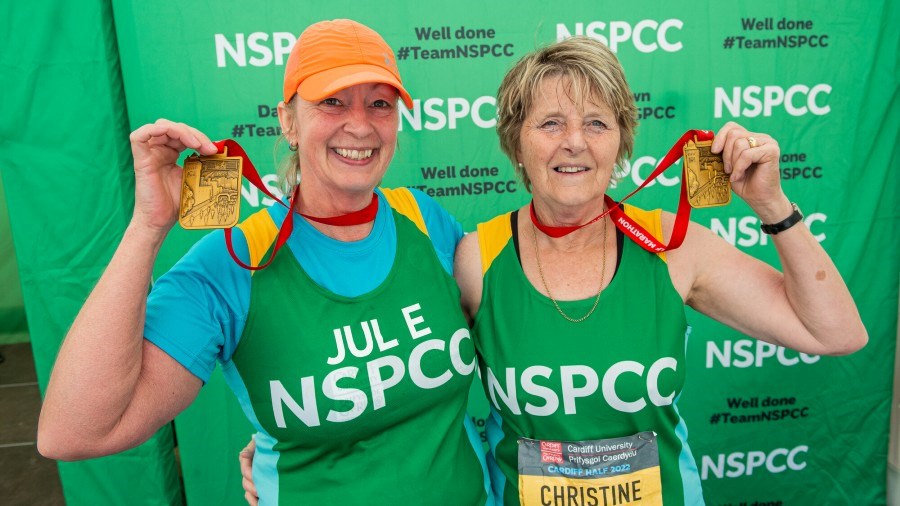 Two Cardiff Half runners in NSPCC vests are in front of the NSPCC stand, holding up their medals