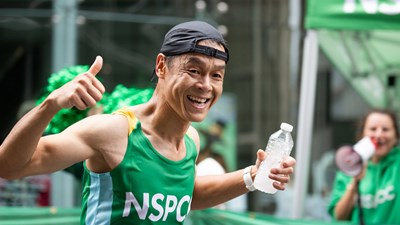A man in a green NSPCC vest running and smiling.
