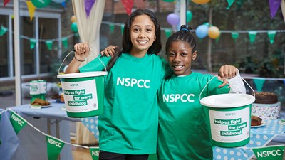 Two teenage girls in NSPCC t-shirts smiling while holding fundraising buckets.