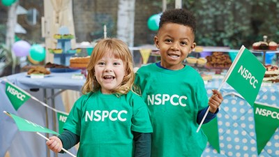 Two young children in green NSPCC t-shirts smiling at the camera.