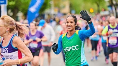 A woman in a green NSPCC vest running and smiling.