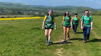 Group of 4 people in NSPCC branded tshirts walking on a hilltop with yellow flowers in the distance