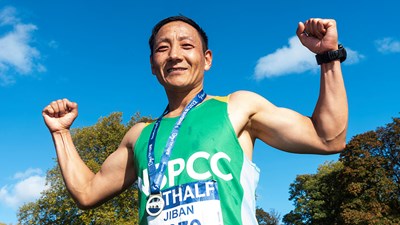 A man in a green NSPCC running vest flexing with his medal.