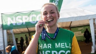 A woman in a green NSPCC running vest biting her medal.