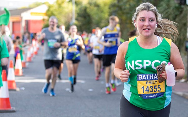 A woman in a green NSPCC vest running and smiling.