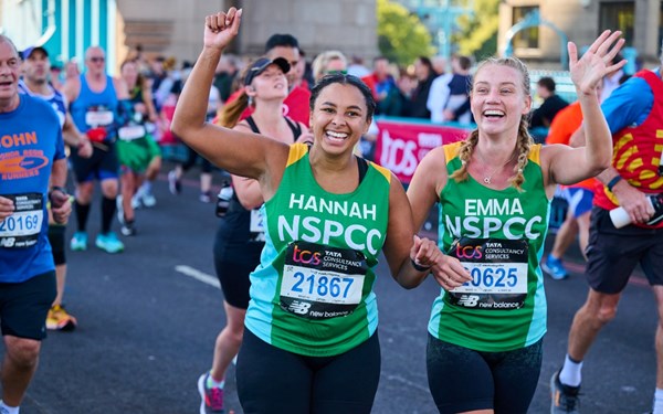 Two women in green NSPCC running vests running and smiling.