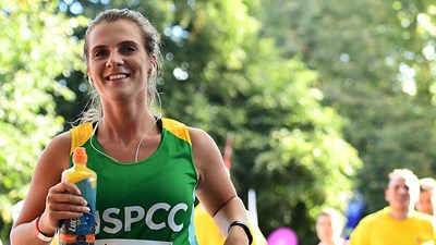 A Team NSPCC member running and smiling during the Royal Parks Half Marathon.