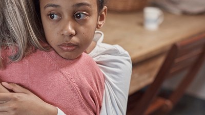 A young child hugging an adult while looking sad.