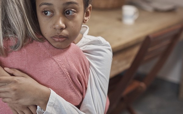 A young child hugging an adult while looking sad.