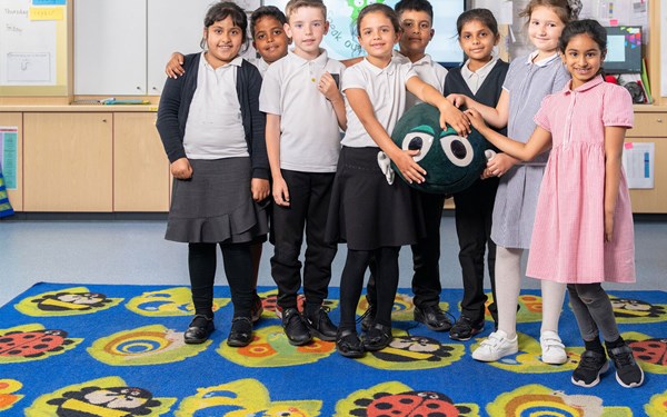 A group of schoolchildren in a classroom holding a toy Buddy