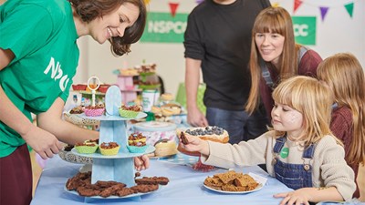 A young girl buying a cake from an NSPCC volunteer.
