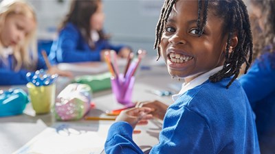 A young boy smiling while drawing at school.