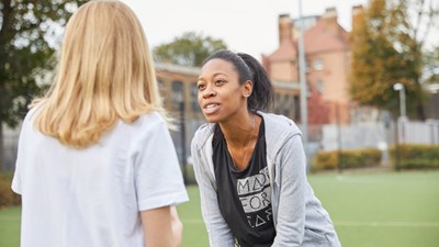 Sports teacher talking to young girl on football pitch