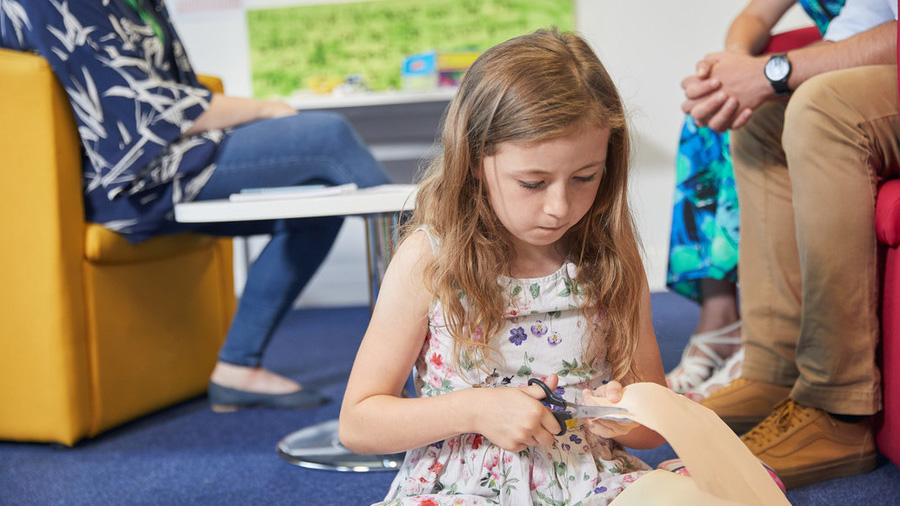 girl sitting on the floor cutting up a piece of paper